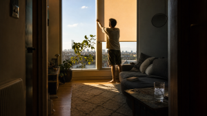 A resident draws a blind across a sun-struck loft window, showing how to keep a home cool in summer UK during a heatwave.